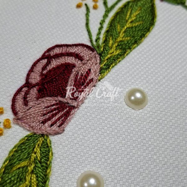 Close up of hand embroidery on white cotton fabric with pink flower and green leaves