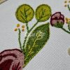Detail of floral hand embroidery on fabric showcasing green leaves and small yellow accents