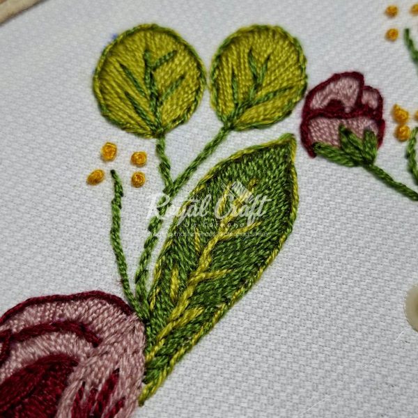 Detail of floral hand embroidery on fabric showcasing green leaves and small yellow accents