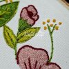 Embroidery detail showing pink and red flowers green leaves and small yellow cluster accents