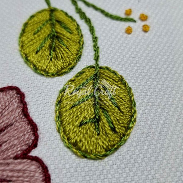 Close-up of beautiful hand embroidered vibrant green leaves on white cotton textile surface texture