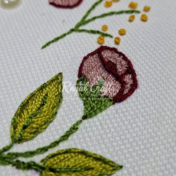 Detailed view of hand embroidered pink flower bud and green leaves against clean white material surface